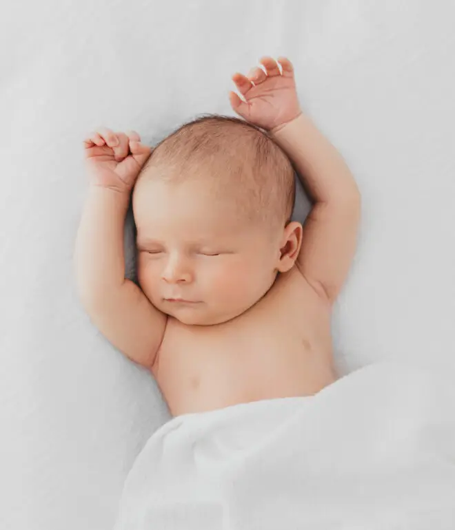 Newborn baby sleeping with his arms above his head and covered with a white blanket Photography Rugby Warwickshire