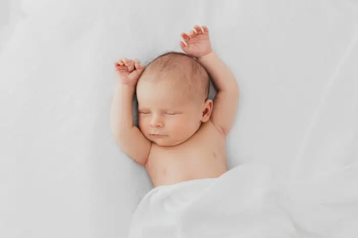 Newborn baby sleeping with his arms above his head and covered with a white blanket Photography Rugby Warwickshire