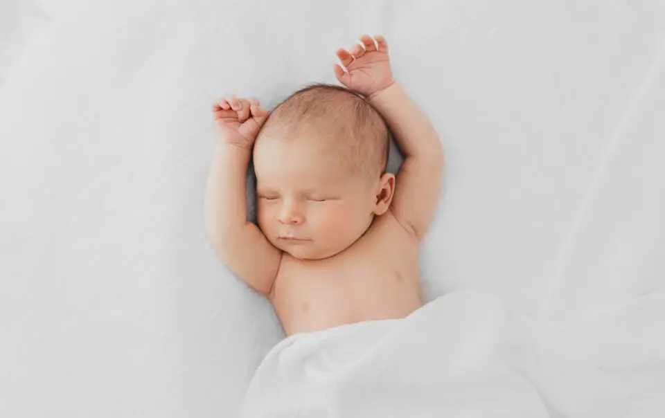 Newborn baby sleeping with his arms above his head and covered with a white blanket Photography Rugby Warwickshire